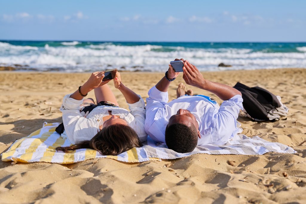 couple lying on beach looking at phones